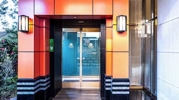 Entrada de hotel com porta de vidro, escada e duas luminárias na parede.