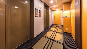 Un pasillo de hotel con piso alfombrado, un ascensor empotrado en la pared y una puerta con el número visible.