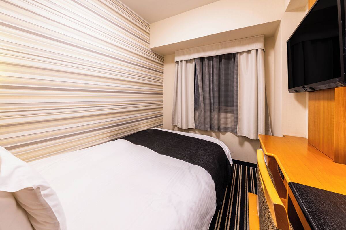 A hotel room with a bed, a desk, a TV, and a window with curtains.