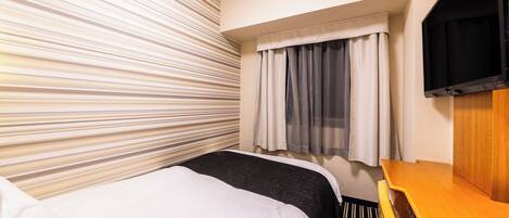 A hotel room with a bed, a desk, a TV, and a window with curtains.