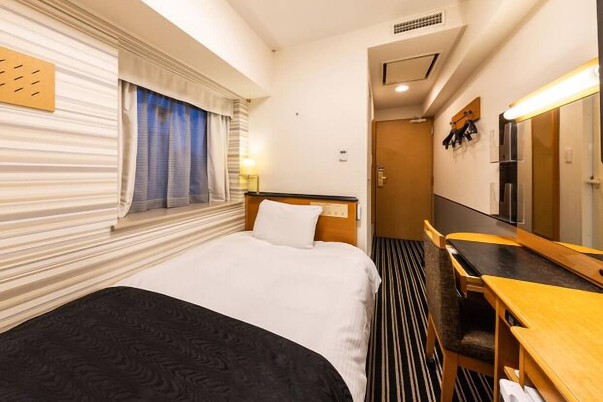 A hotel room with a bed, a desk, a mirror, and a window with curtains.