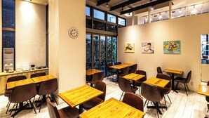 Un comedor moderno con mesas y sillas de madera, ventanas amplias y obras de arte en las paredes.