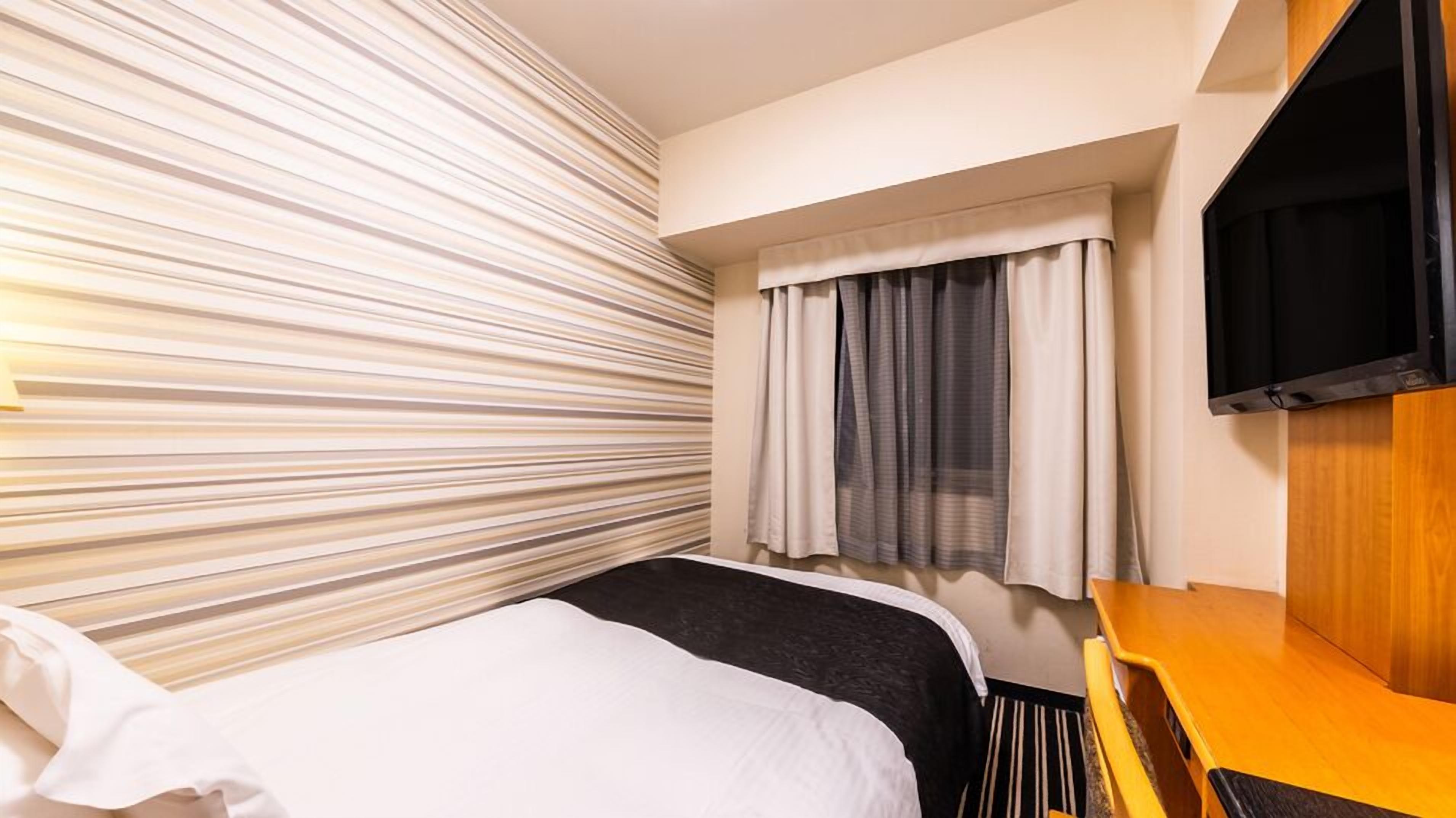 A hotel room with a bed, a TV, a window with curtains, and a striped wall.