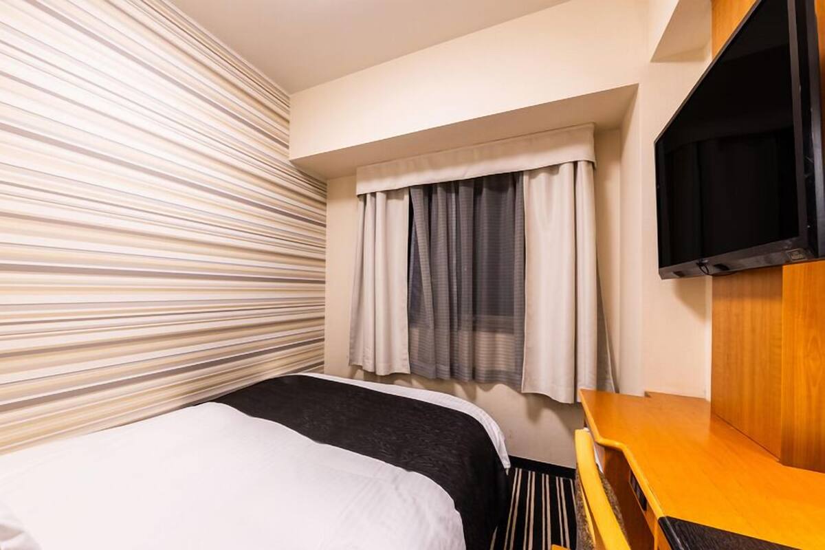 A hotel room with a bed, a TV, a window with curtains, and a striped wall.