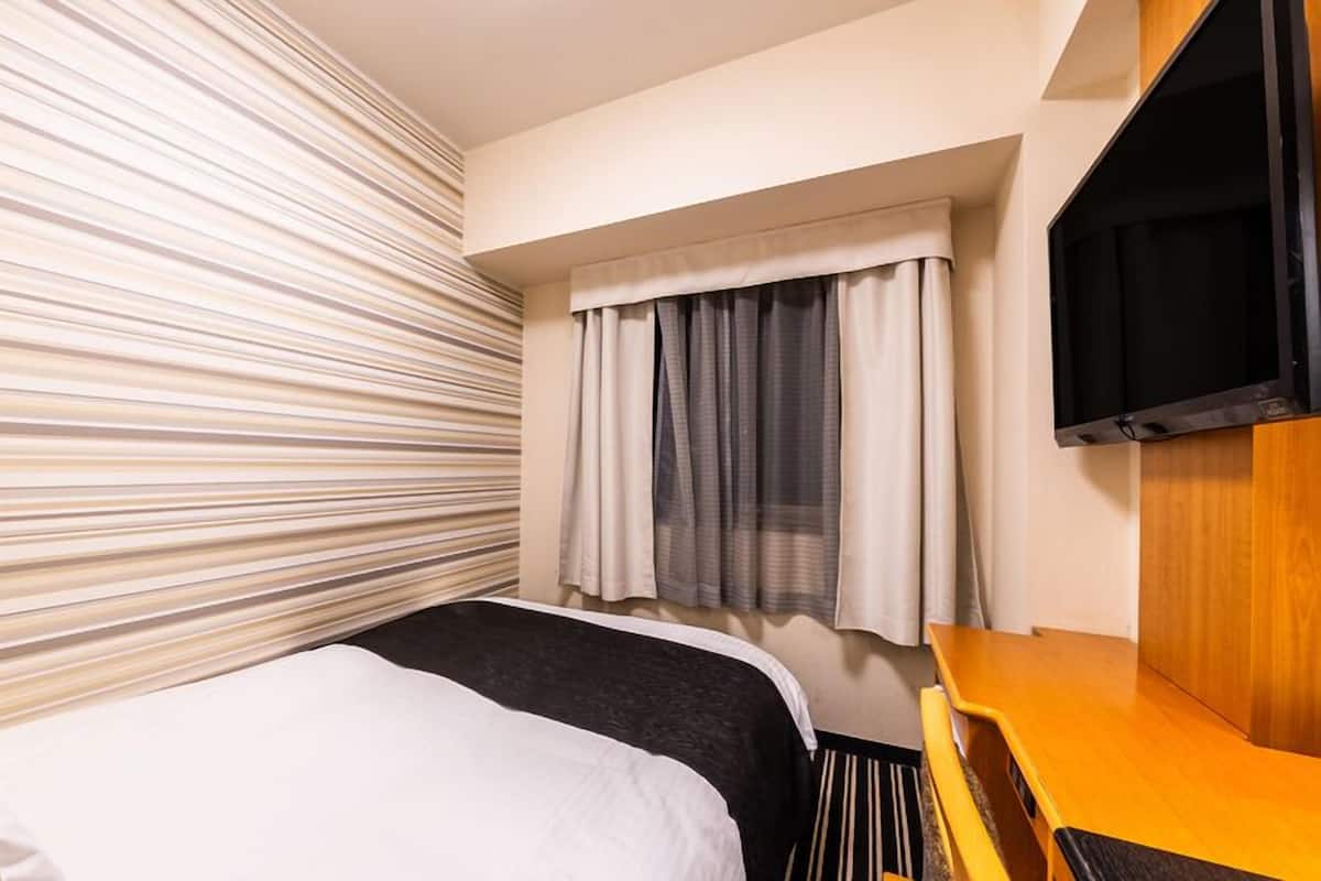 Quarto de hotel com uma cama, televisão, janela com cortinas e parede listrada.