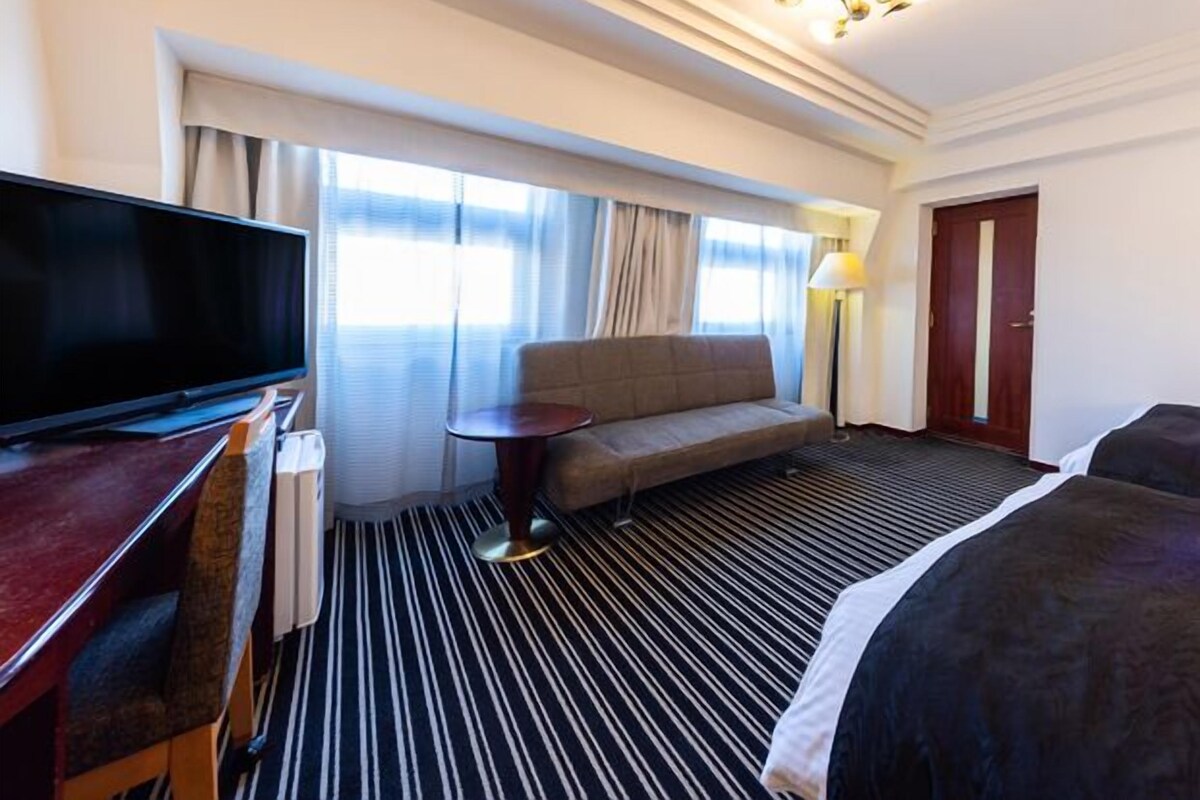 A hotel room with a flat-screen TV, a sofa, a small table, a lamp, and a bed.