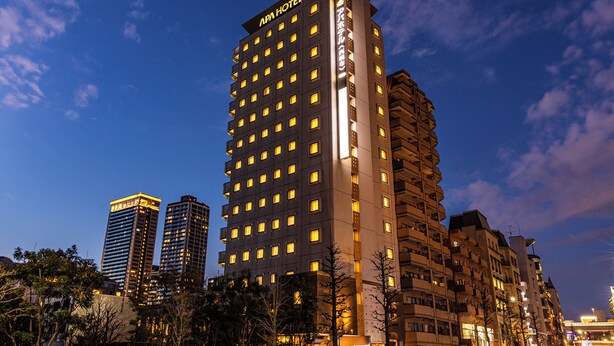 Un hotel de varios pisos con un letrero llamativo en la parte superior, rodeado de otros edificios y árboles.
