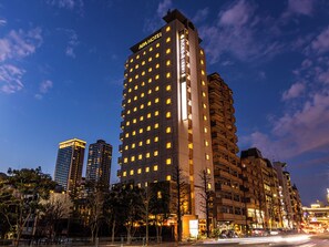 A multi-story hotel with a prominent sign at the top, surrounded by other buildings and trees. - APA Hotel Nishiazabu (Tokyo)