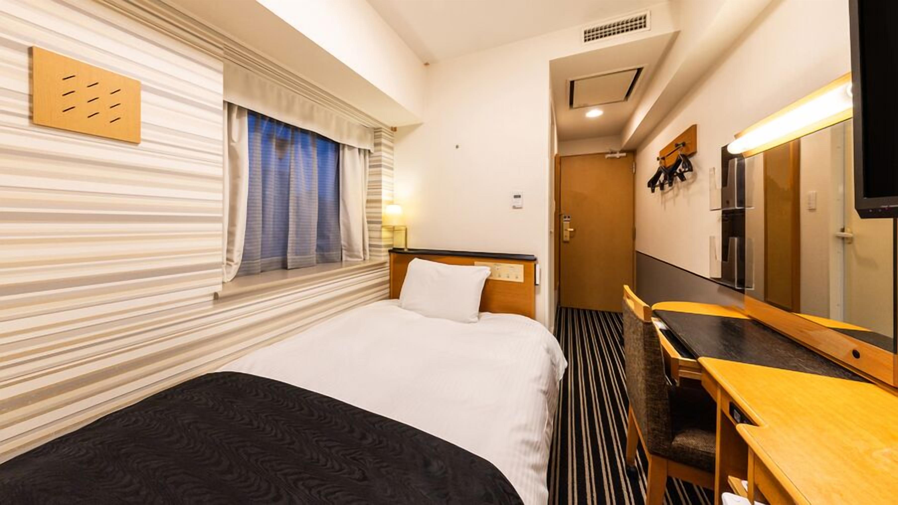 A hotel room with a bed, a desk, a mirror, and a window with curtains.