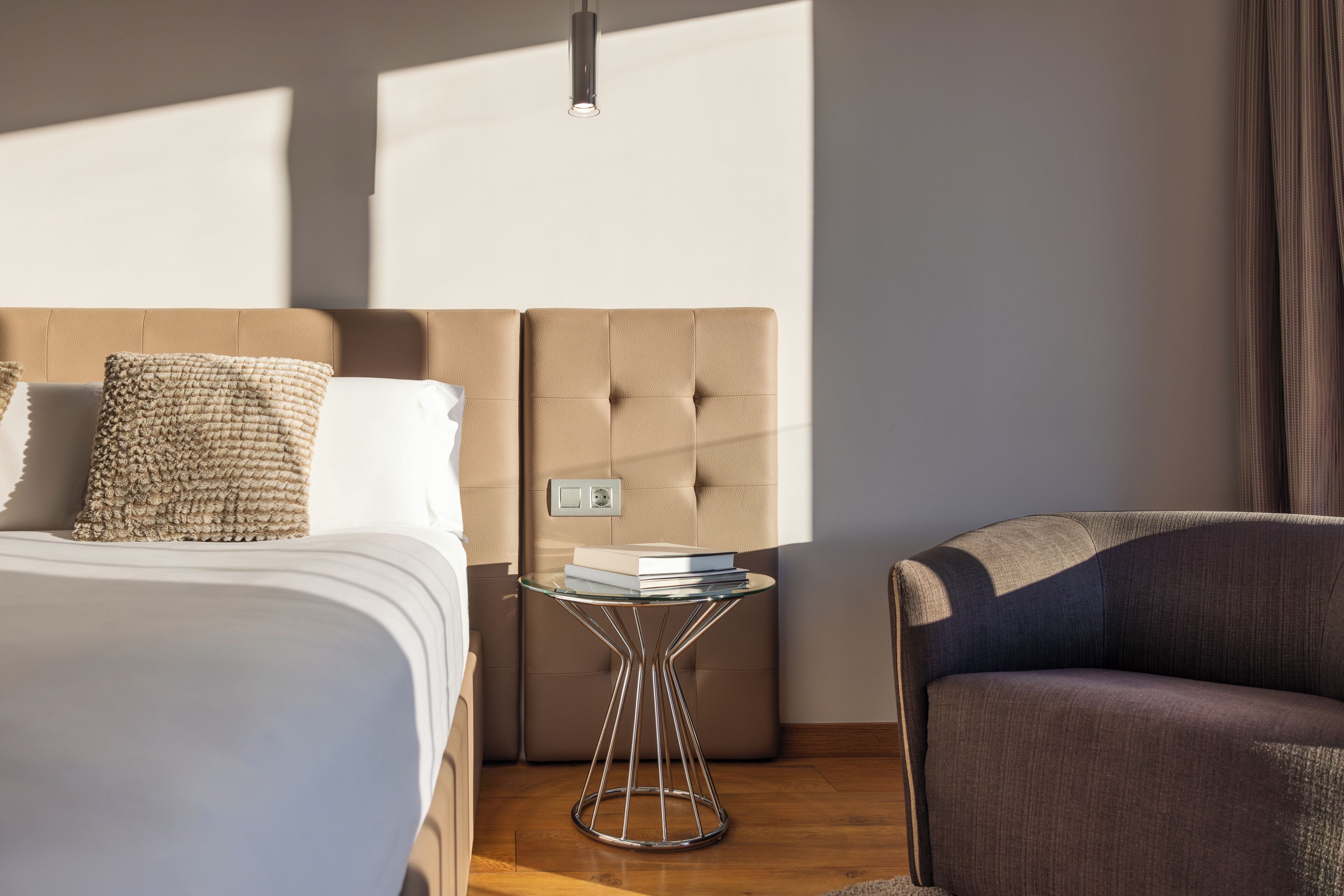 Une chambre d’hôtel moderne, dotée d’un grand lit, d’une petite table de chevet, d’une chaise et d’un luminaire fixé au mur.