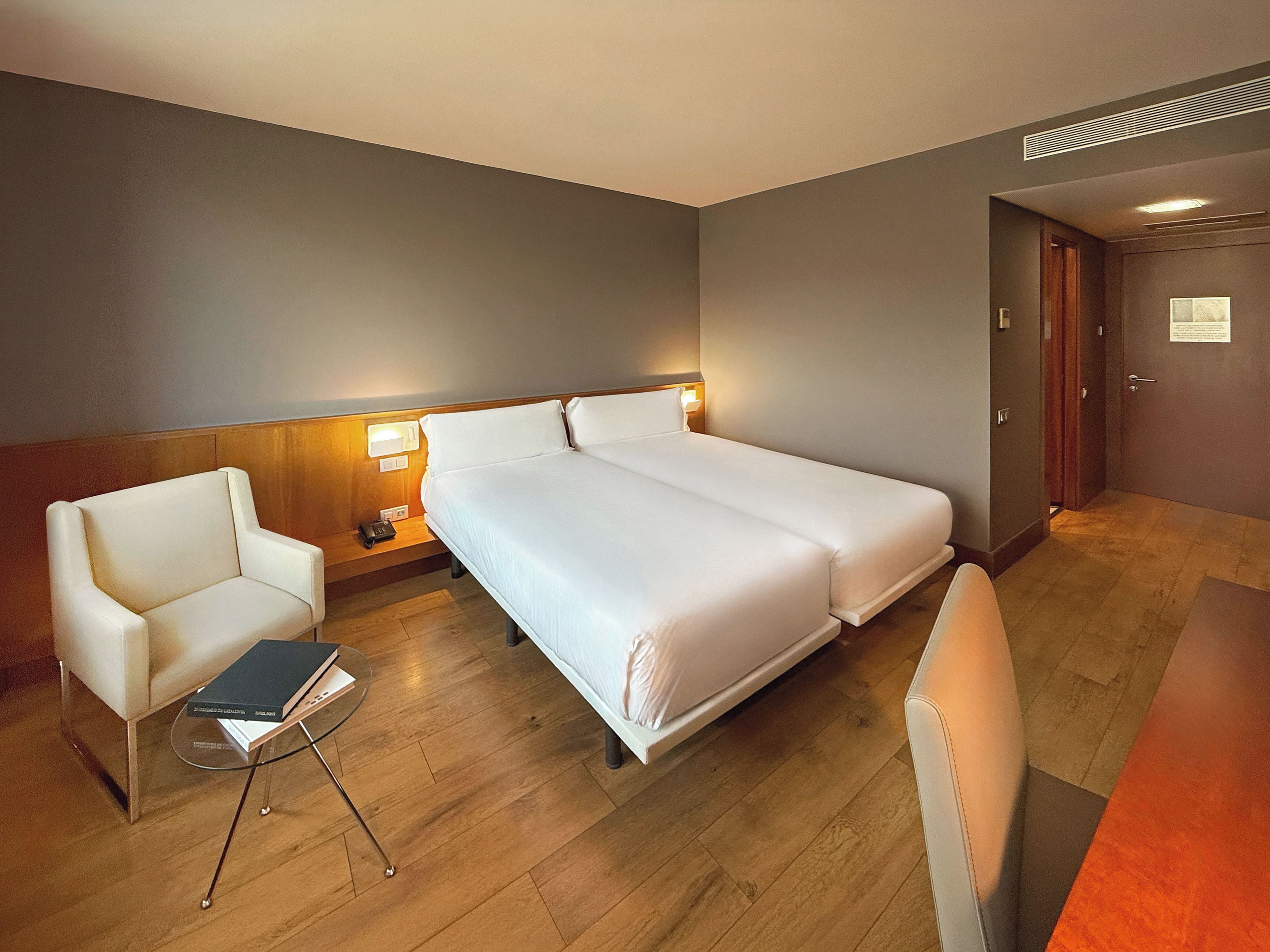 A hotel room with a bed, a chair, a small table, and a desk.