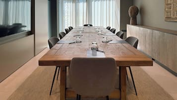 Un salón de conferencias con una larga mesa de madera, sillas negras y un amplio ventanal con cortinas translúcidas.