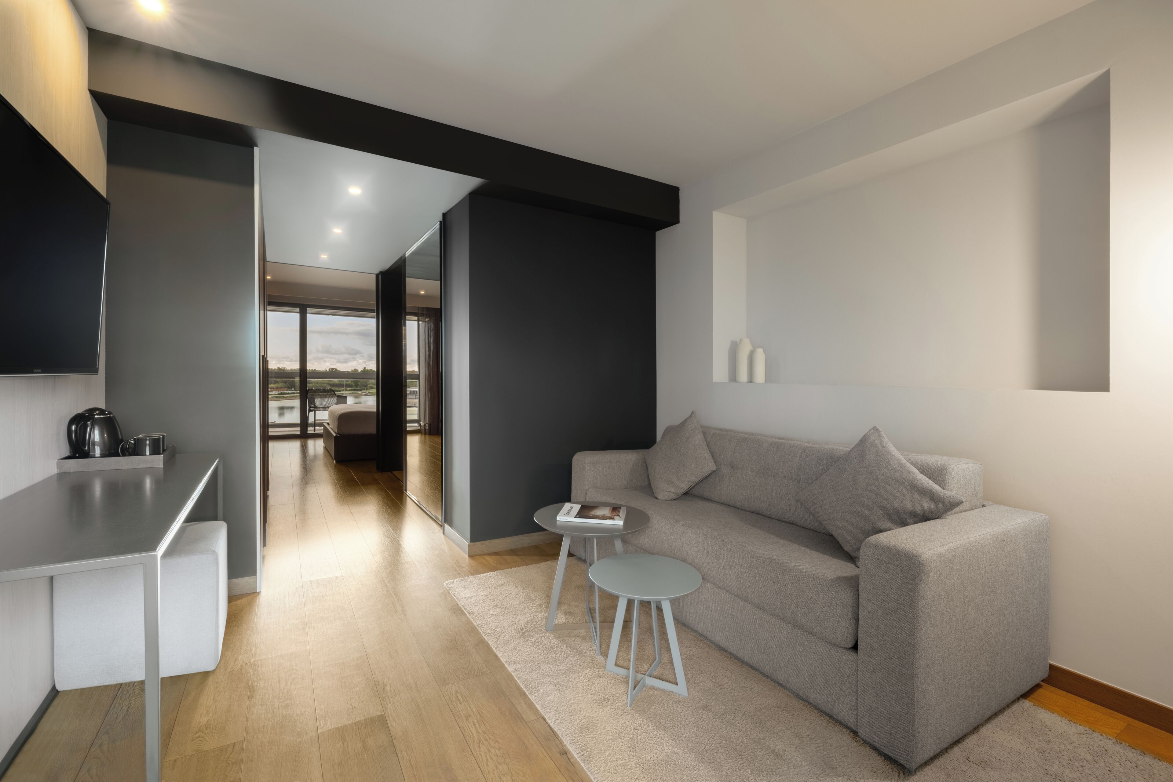 A modern living room with a grey sofa, a small round table, and a kitchen area with a white countertop.