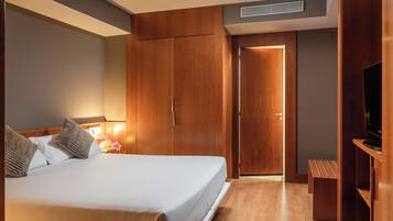 Habitación de hotel con cama, armario de madera, televisor y un banco.