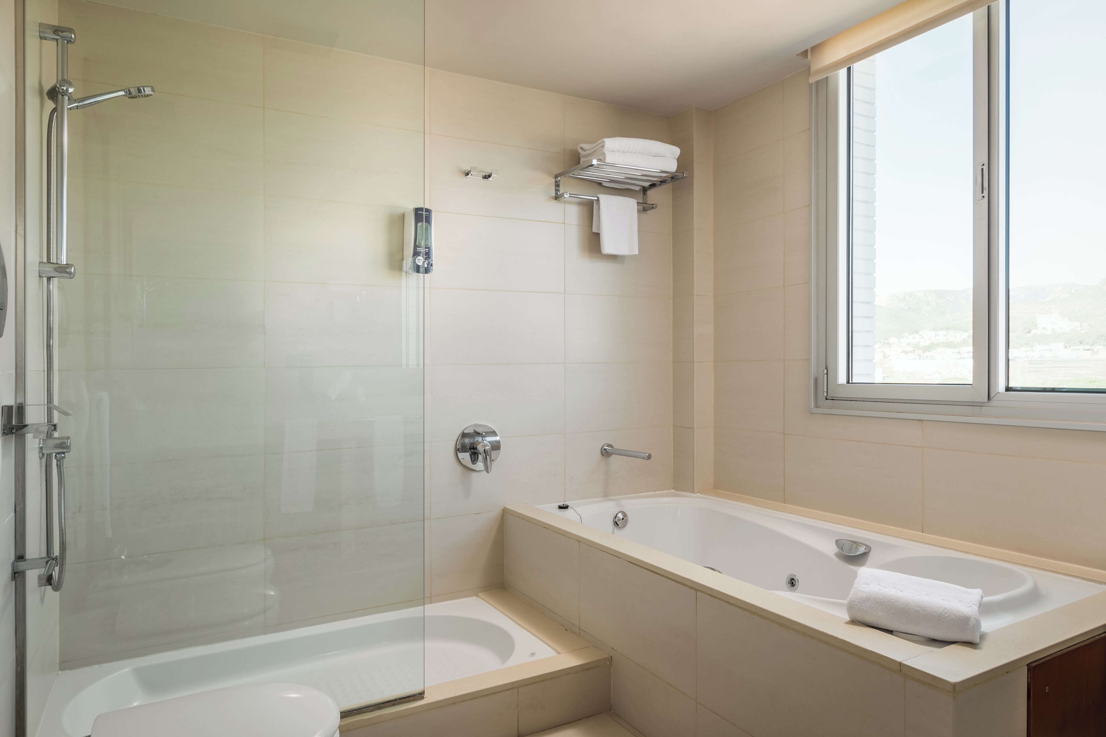 A modern bathroom with a glass-enclosed shower, a freestanding bathtub, and a vanity with a window.