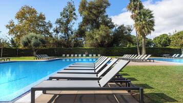 Piscina con sillas de descanso, rodeada de árboles y un cielo despejado.