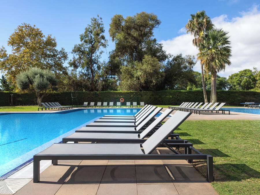 Piscina con sillas de descanso, rodeada de árboles y un cielo despejado.