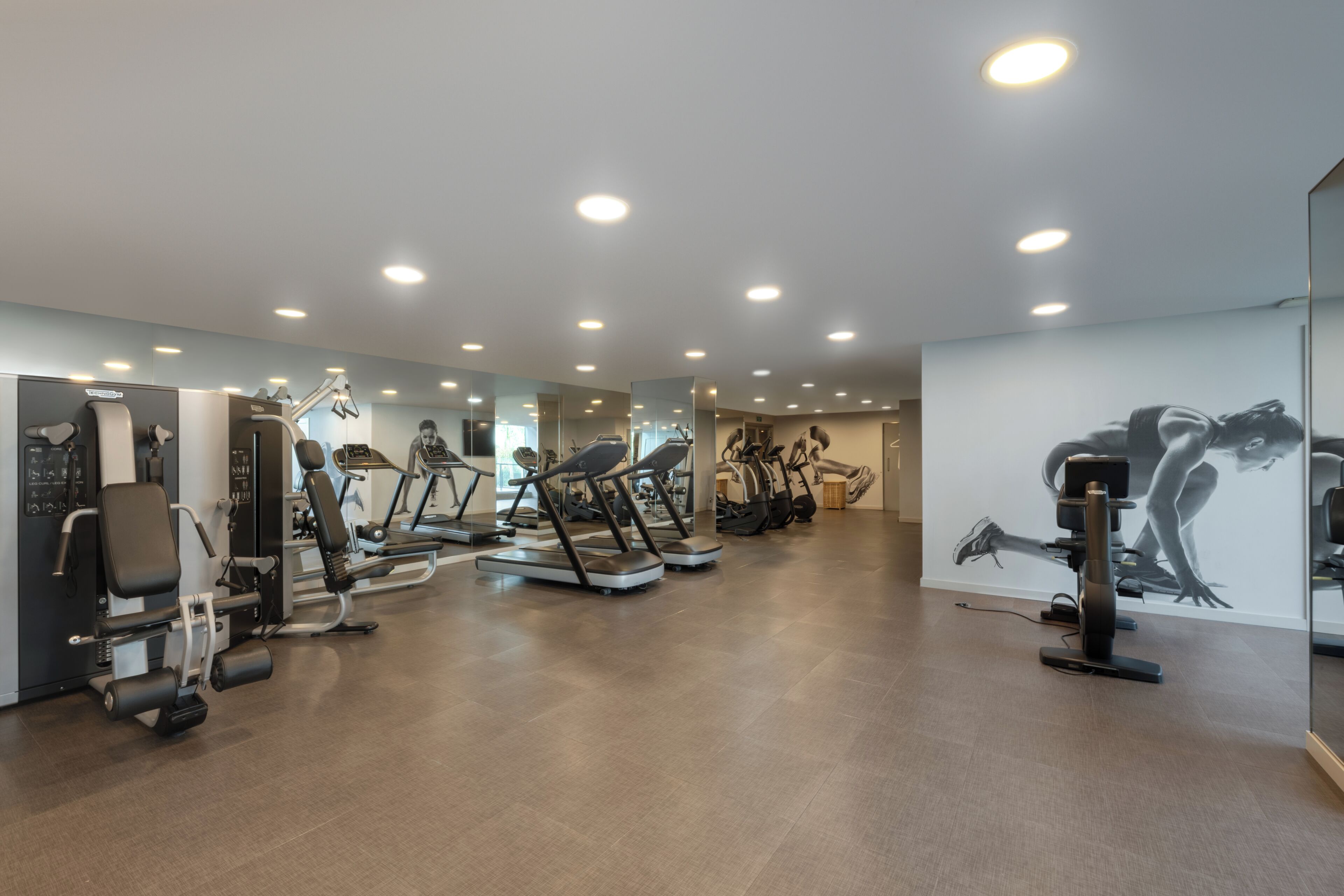A gym with various exercise machines, a mirrored wall, and a large artwork.