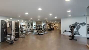 A gym with various exercise machines, a mirrored wall, and a large artwork.