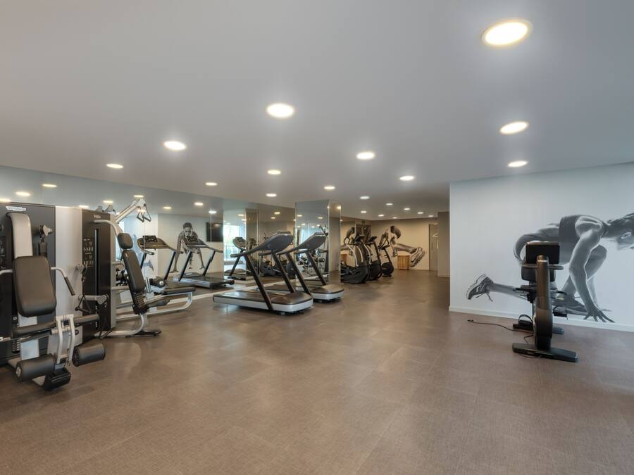 A gym with various exercise machines, a mirrored wall, and a large artwork.