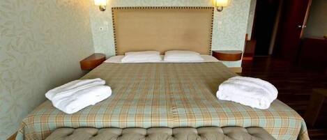 A large bed with a headboard, two bedside tables, and two wall-mounted lamps.