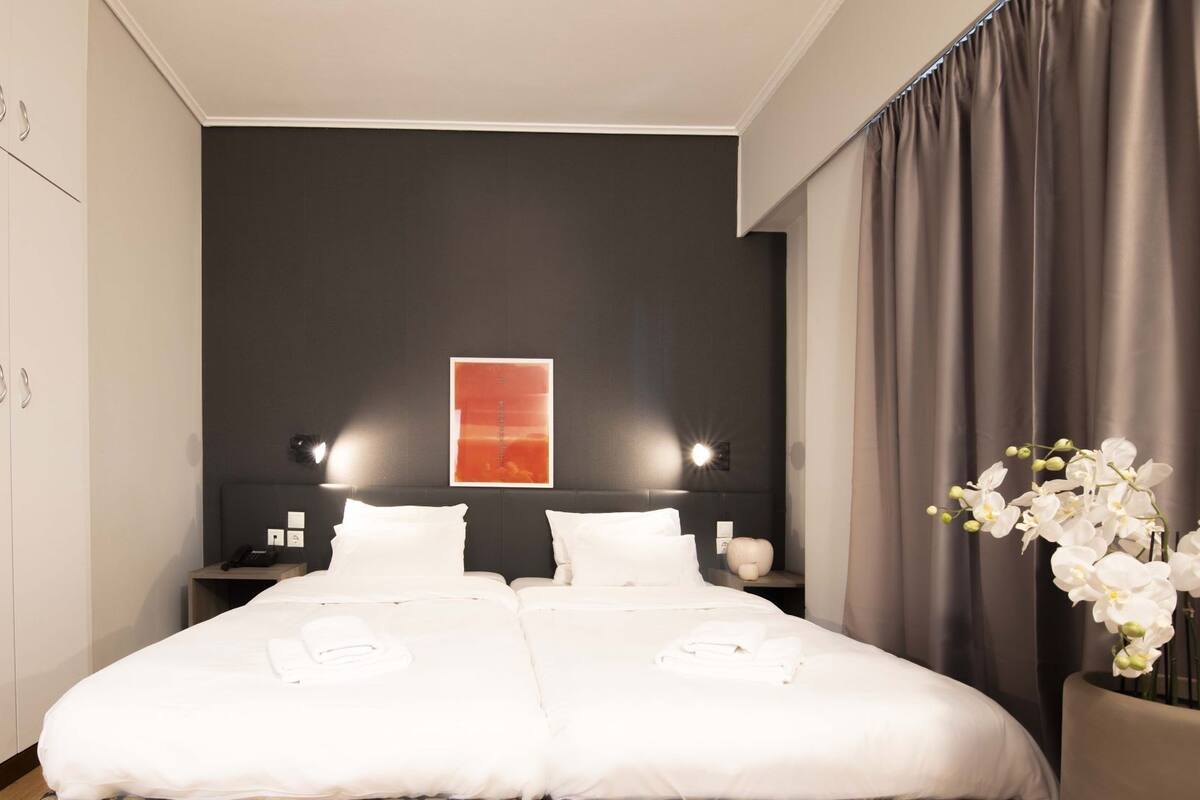 Habitación de hotel con una cama grande, dos mesitas de noche, una obra de arte colgada en la pared y un jarrón con flores blancas.