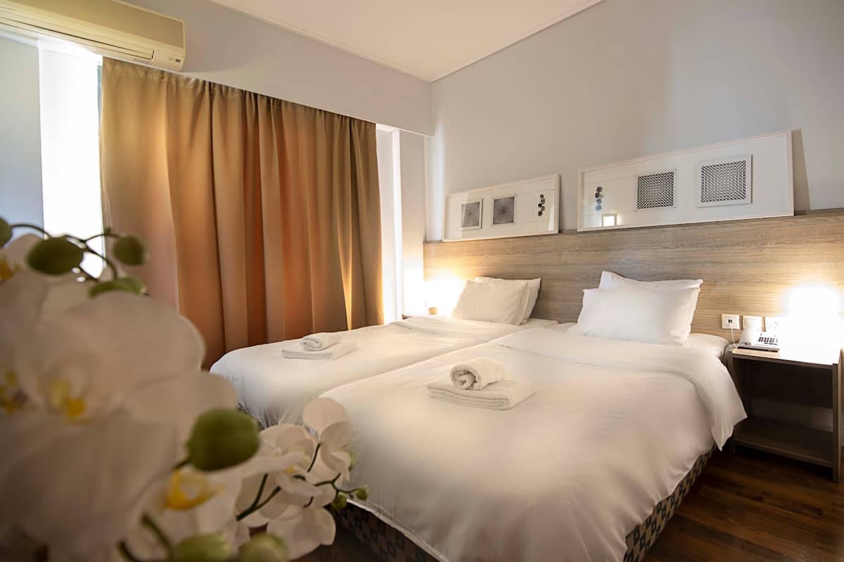 Habitación de hotel con dos camas, cabecero de madera, mesita de noche con teléfono y ventana con cortinas.