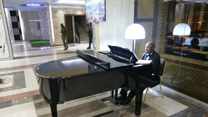 Un piano de cola en un vestíbulo amplio con diseño moderno, un espejo grande y una escalera al fondo.