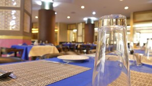 Un comedor con mesas dispuestas para dos, cristalería transparente y posavasos tejidos.