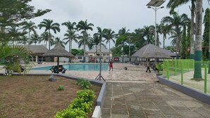 Un área de piscina con palmeras, sillones de descanso y un edificio al fondo.