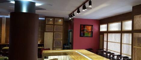 Un restaurante con una mesa de madera en el centro, asientos a ambos lados y una pared decorada con un cuadro colorido.