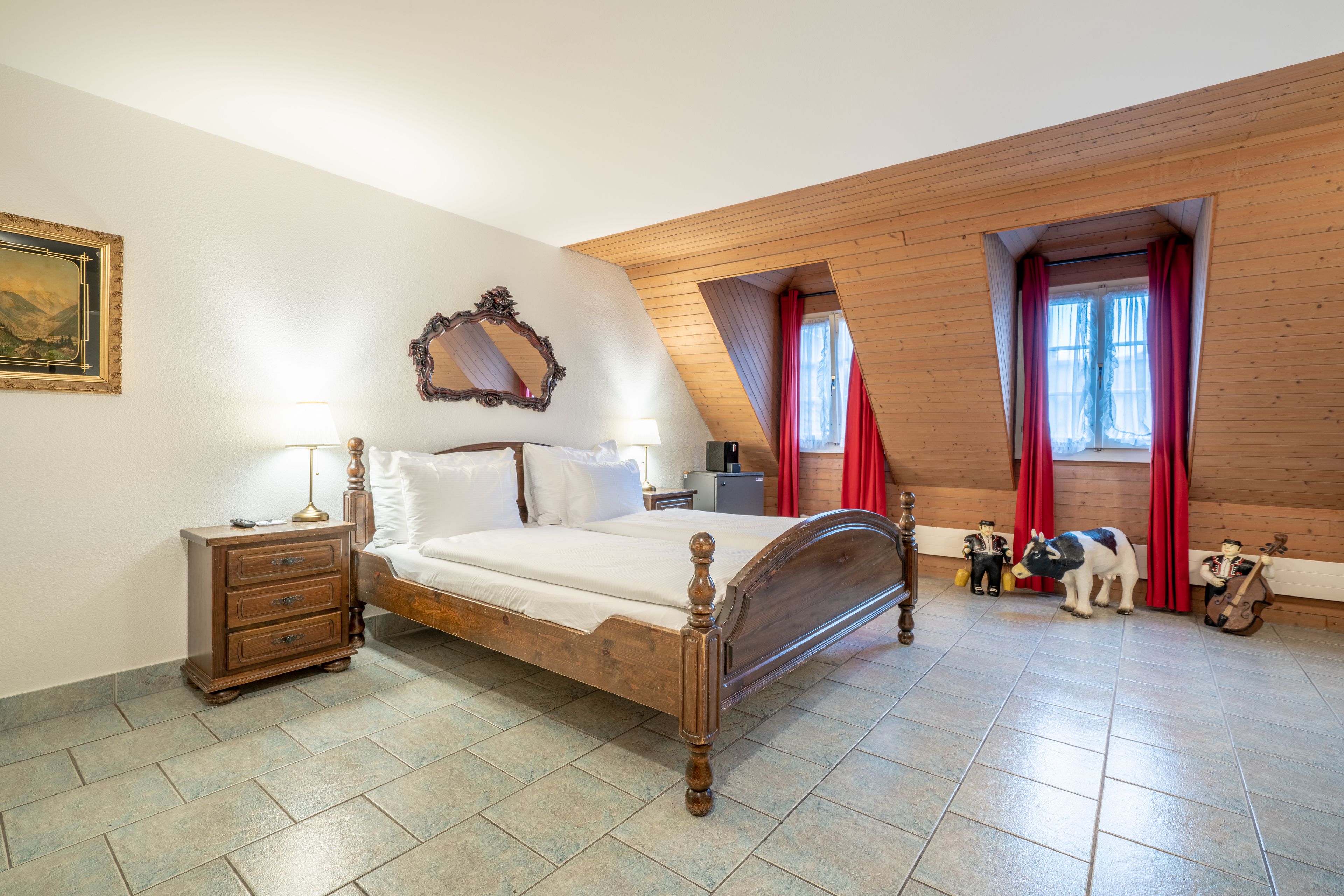 Un dormitorio con cama de madera, cómoda, mesita de noche, espejo y ventana con cortinas rojas.