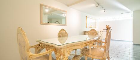 Un coin repas agrémenté de meubles décoratifs, d’une table à plateau en verre et de deux miroirs fixés au mur.