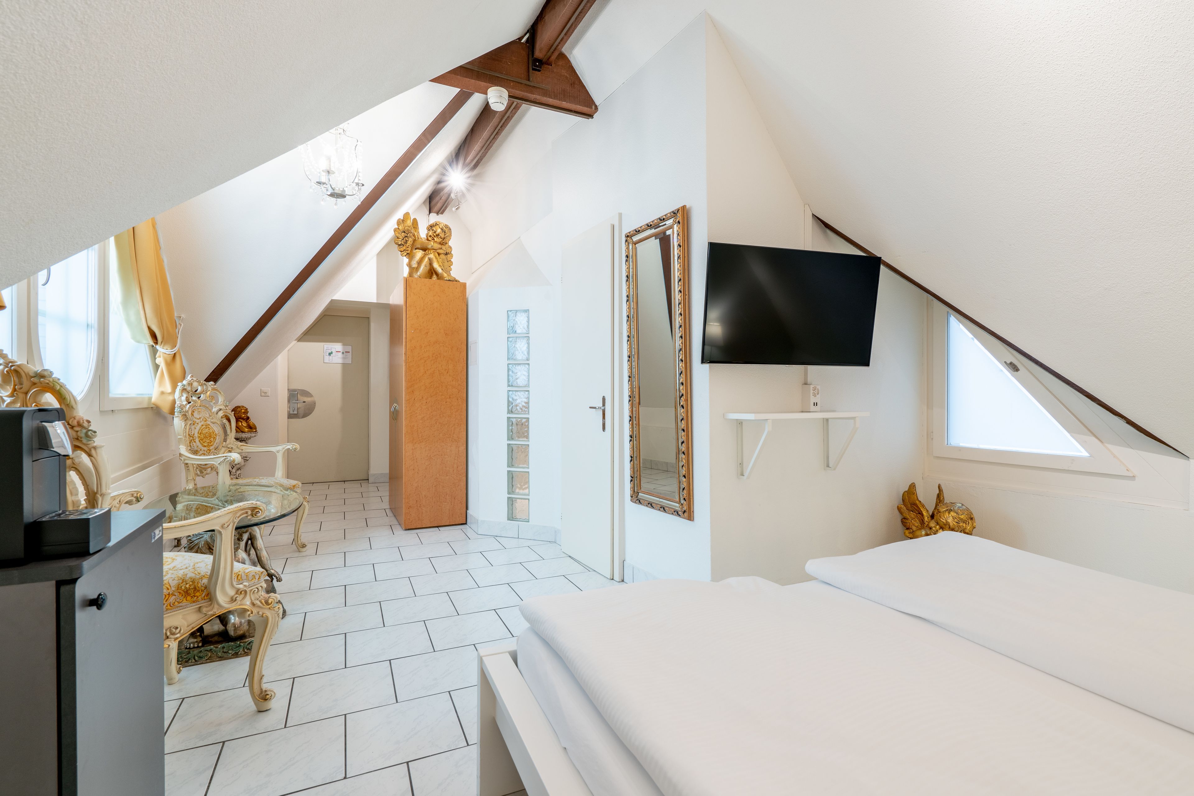Un dormitorio con techo inclinado, una cama, un televisor y muebles ornamentales.