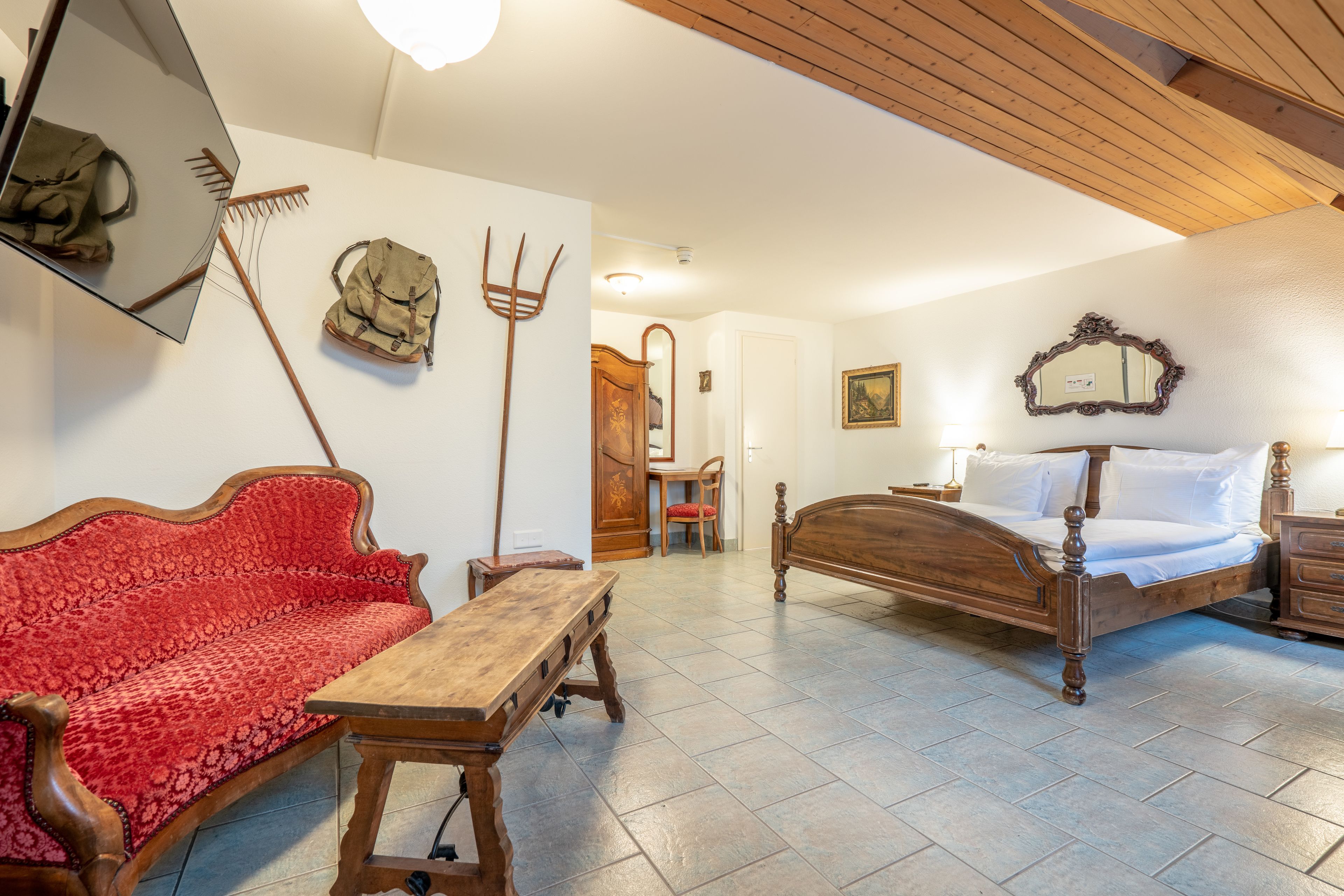 Una habitación con una cama de madera, un sofá rojo, una mesa de madera, un espejo y un techo de madera.