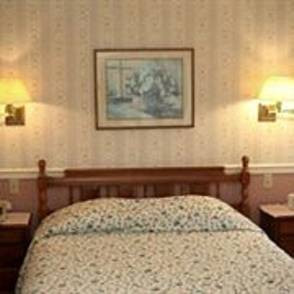 A hotel room with a wooden bed, a framed picture on the wall, and two bedside lamps. - Soldotna Alaska Fishing Lodge (Soldotna)