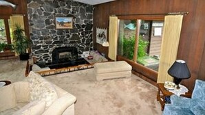 A living room with a stone wall, a fireplace, a sofa, and a window with curtains. - Soldotna Alaska Fishing Lodge (Soldotna)