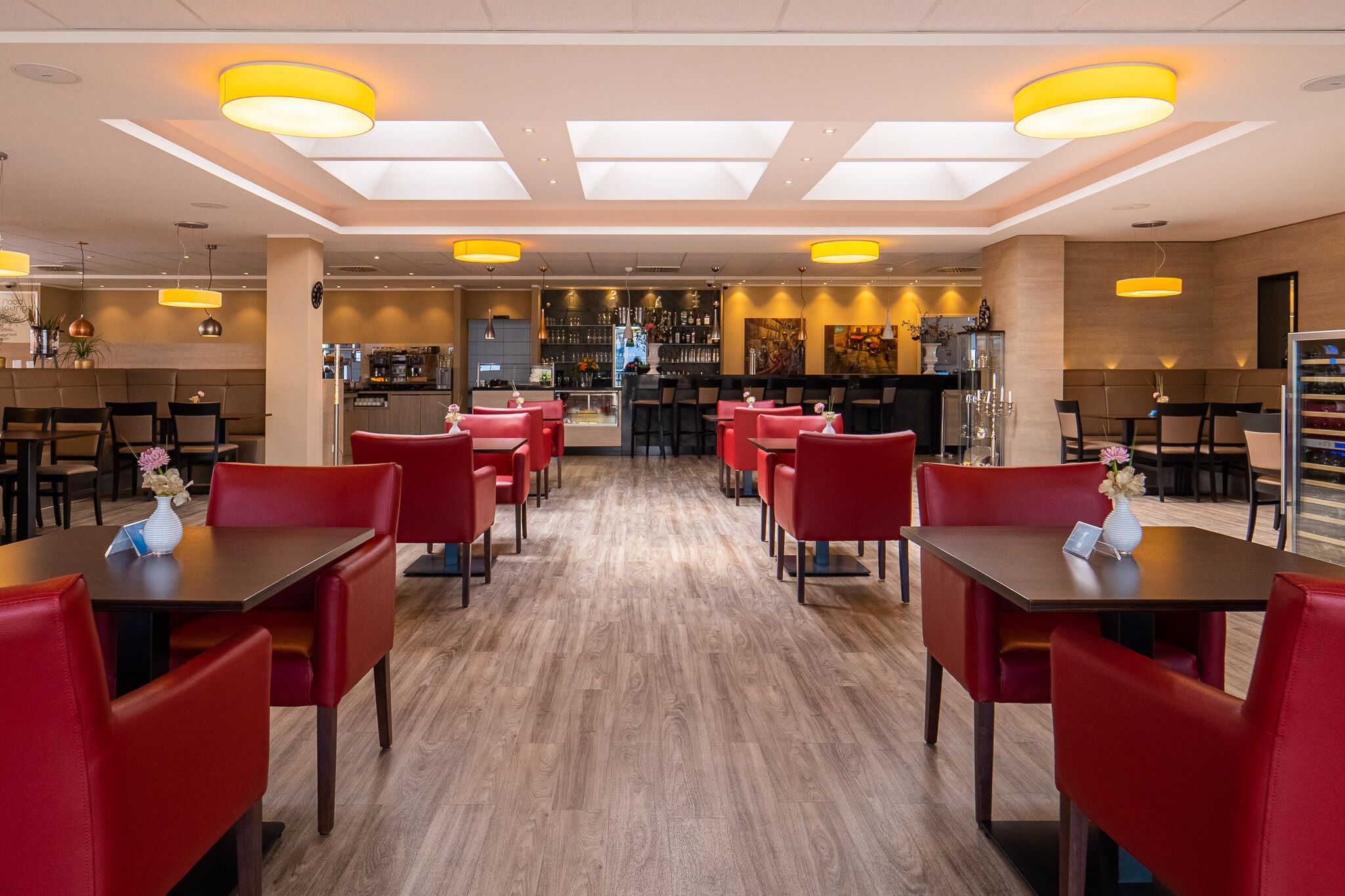 Un restaurante moderno con sillas y mesas rojas, una zona de bar y suelo de madera.