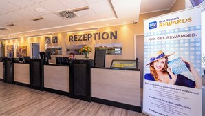 A reception area with a reception desk, a large sign advertising Best Western Rewards, and a view of the lobby. - Hotel Maximilian (Weil am Rhein)