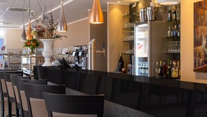 A bar area with a counter, bar stools, and a refrigerator stocked with bottles. - Hotel Maximilian (Weil am Rhein)