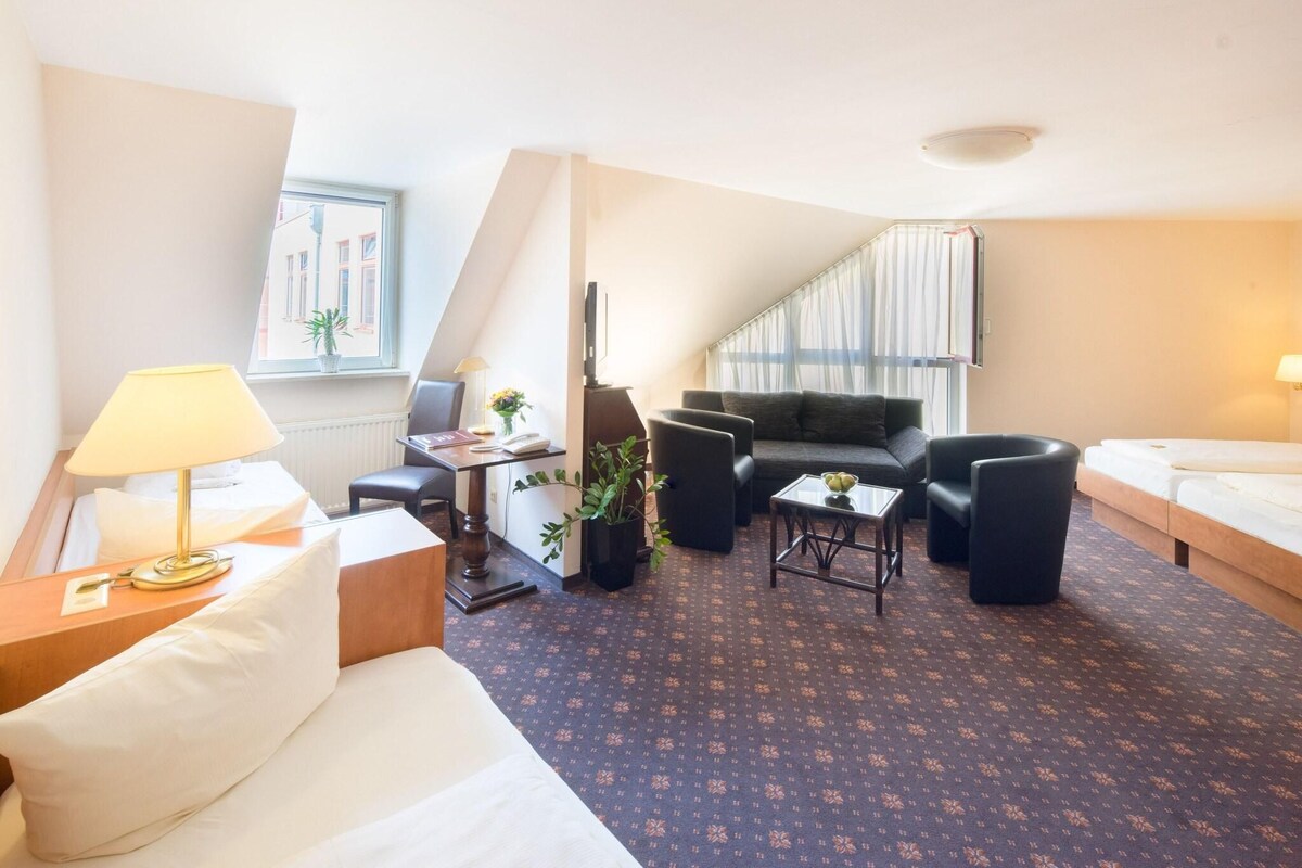 Ett hotellrum med en soffa, ett matbord, ett soffbord, en tv och en trappa.