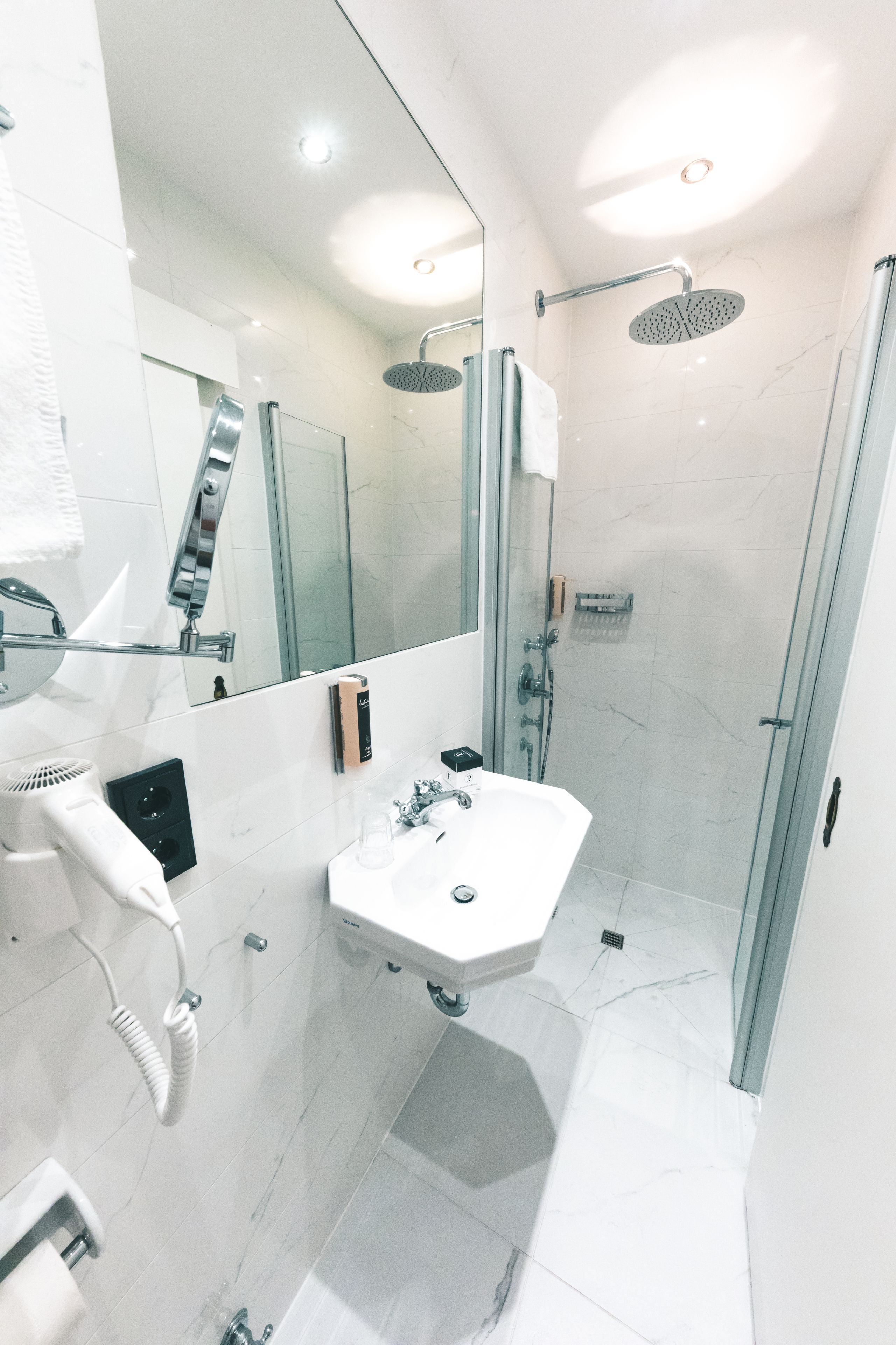 A modern bathroom with a glass-enclosed shower, a white sink, and a large mirror.