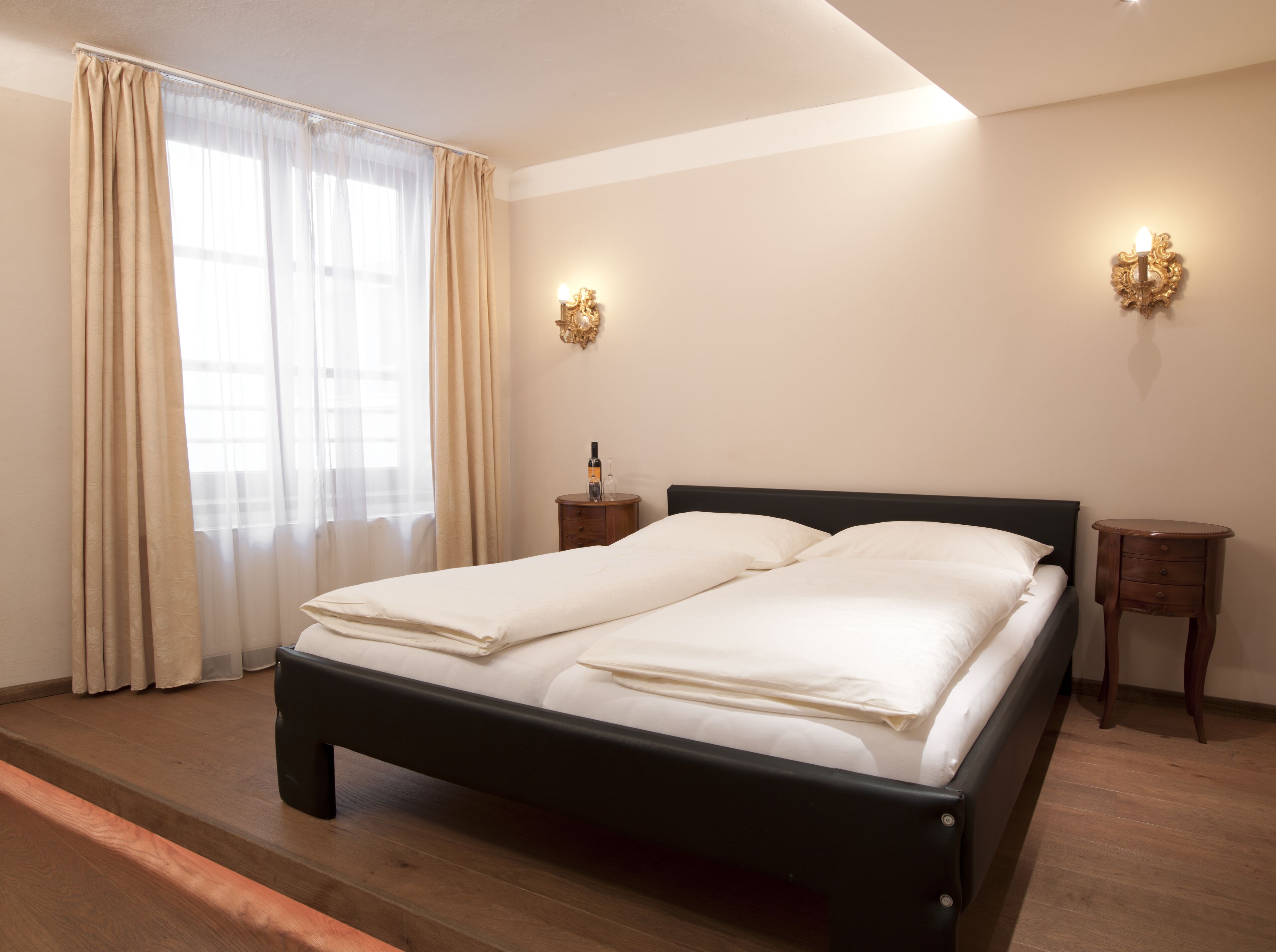 Una cama bien hecha con sábanas blancas, cabecera de madera y dos mesitas de noche con lámparas.