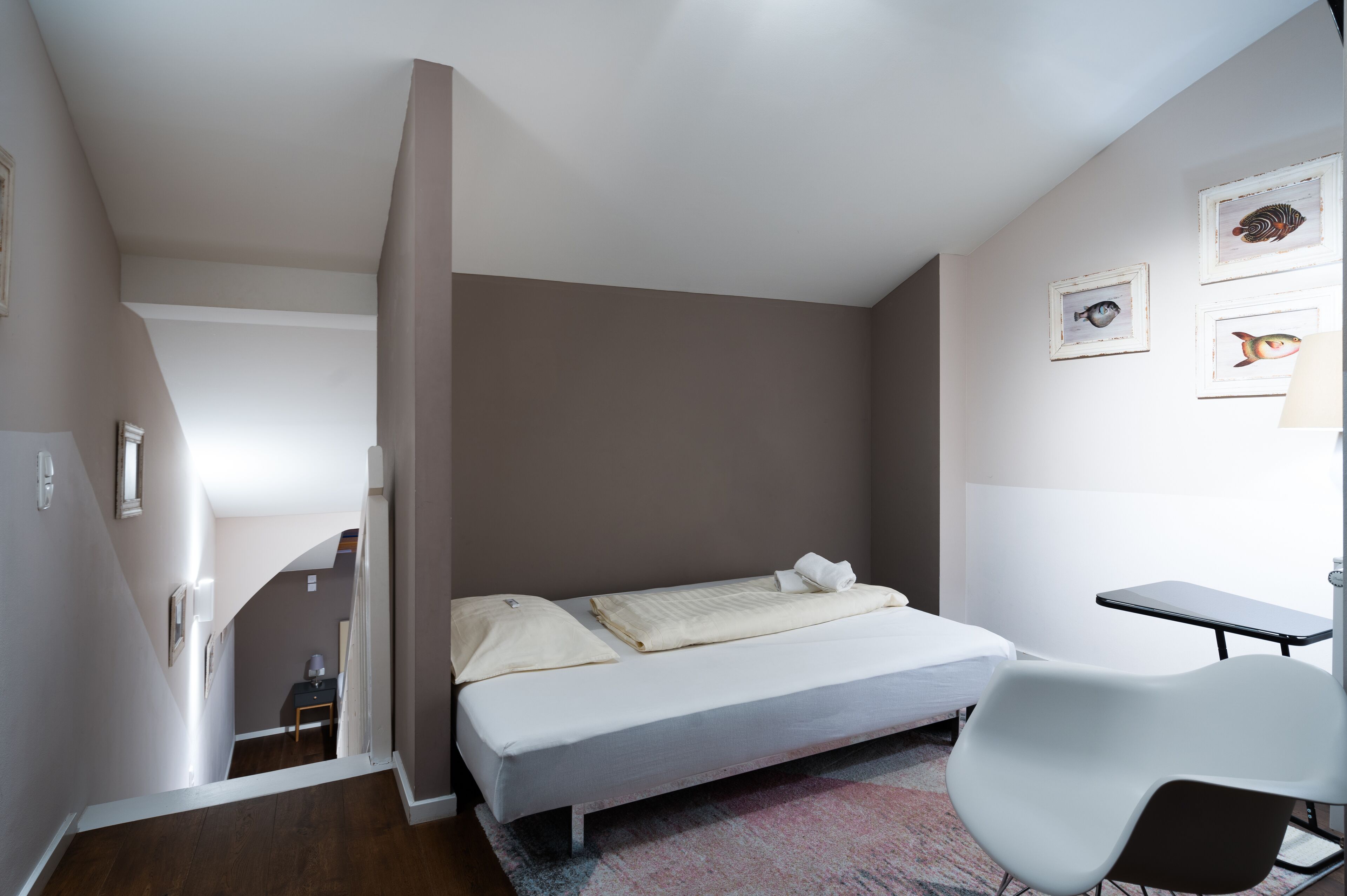 Una camera da letto con un letto, una sedia e una scrivania. Una scala conduce a un'altra stanza.