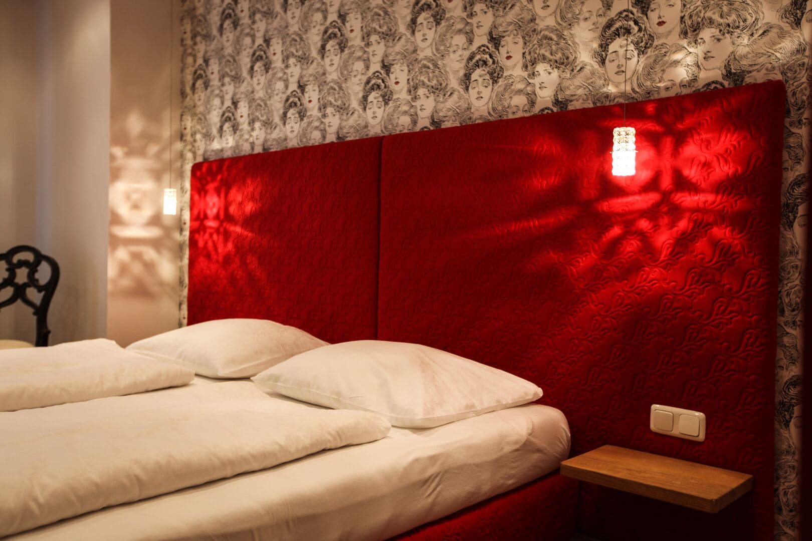 Un letto con biancheria bianca e una testiera rossa con una lampada.