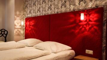 Un lit avec une literie blanche et une tête de lit rouge agrémentée d’un luminaire.