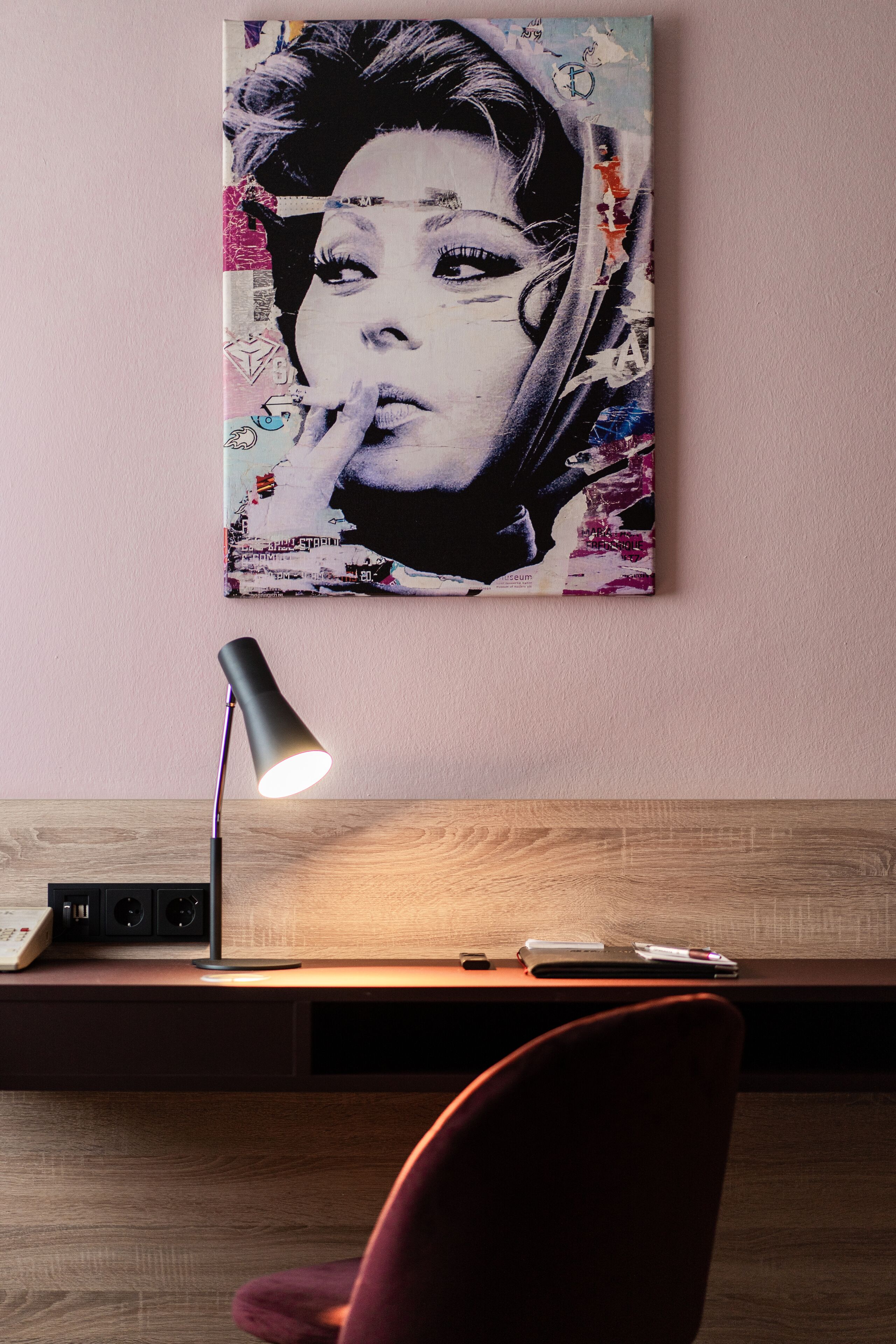 Een bureau met een lamp, een stoel en een kunstwerk aan de muur.