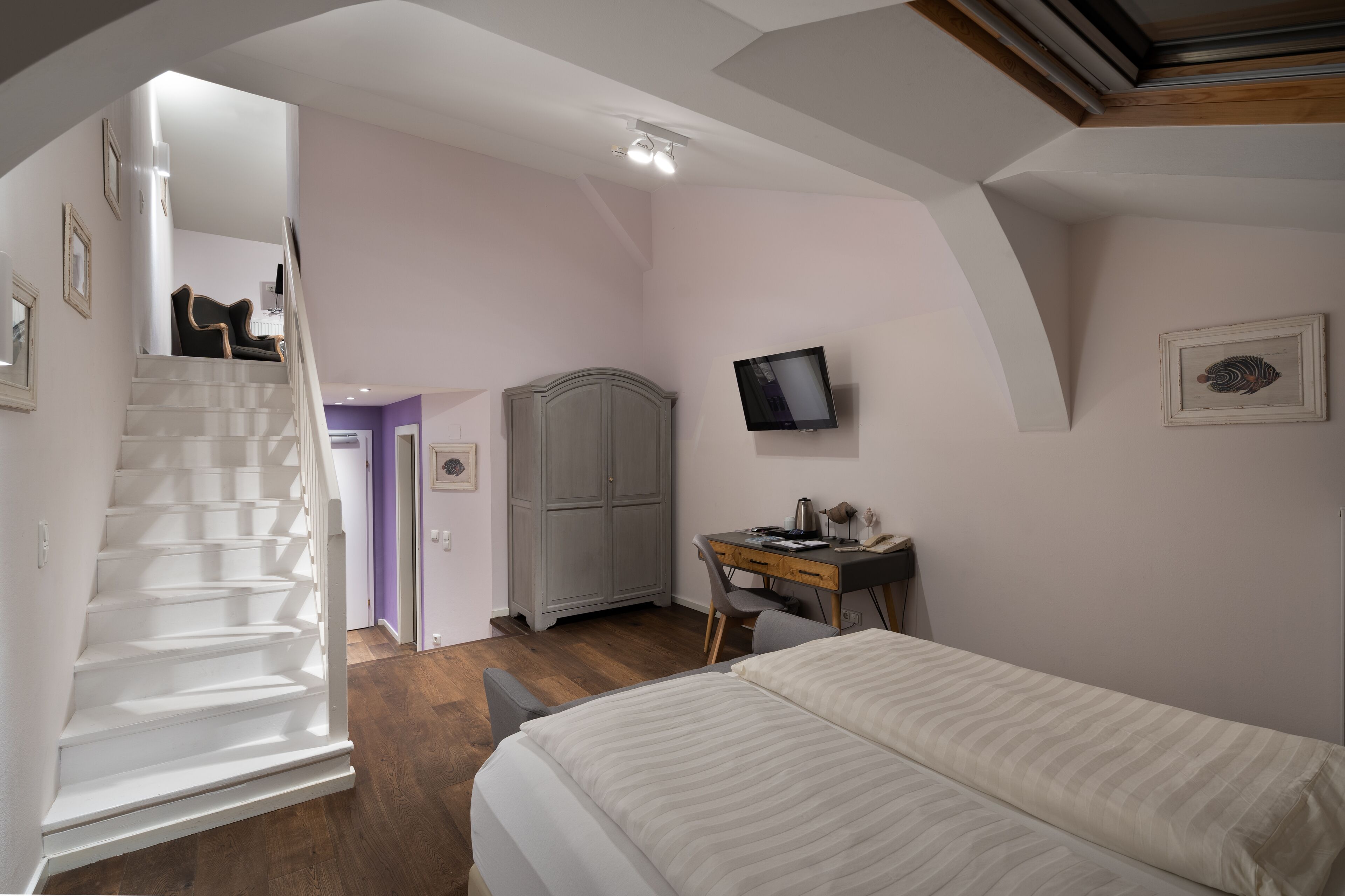 A bedroom with a bed, a desk, a chair, a wardrobe, and a staircase leading to another room.