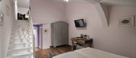 A bedroom with a bed, a desk, a chair, a wardrobe, and a staircase leading to another room.