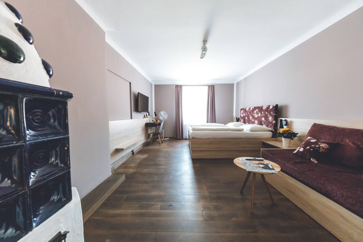 A modern hotel room with a wooden floor, a sofa, a bed, a TV, and a small table with a magazine.